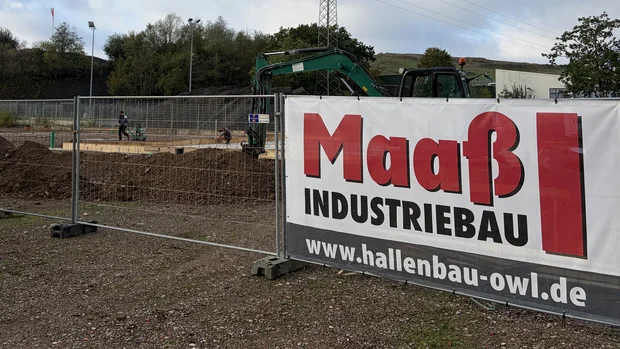 Baustelle der neuen Produktionshalle für Orthopädietechnik mit Erdarbeiten, Bagger und Maaß-Industriebau-Bauschild