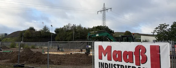 Produktionshalle für Orthopädietechnik im Bau Baustelle der neuen Produktionshalle für Orthopädietechnik mit Erdarbeiten, Bagger und Maaß-Industriebau-Bauschild