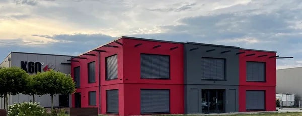 Außenansicht des zweigeschossigen K60-Bürogebäudes in Langenberg mit roter Fassade und grauem Eingangsbereich